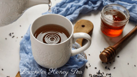 Lavender Tea Time Recipe featured image showing A white mug of lavender honey tea being poured from a teapot. A jar of honey, a honey dipper, and dried lavender flowers are scattered around the mug on a wooden board Lemon and Sophia
