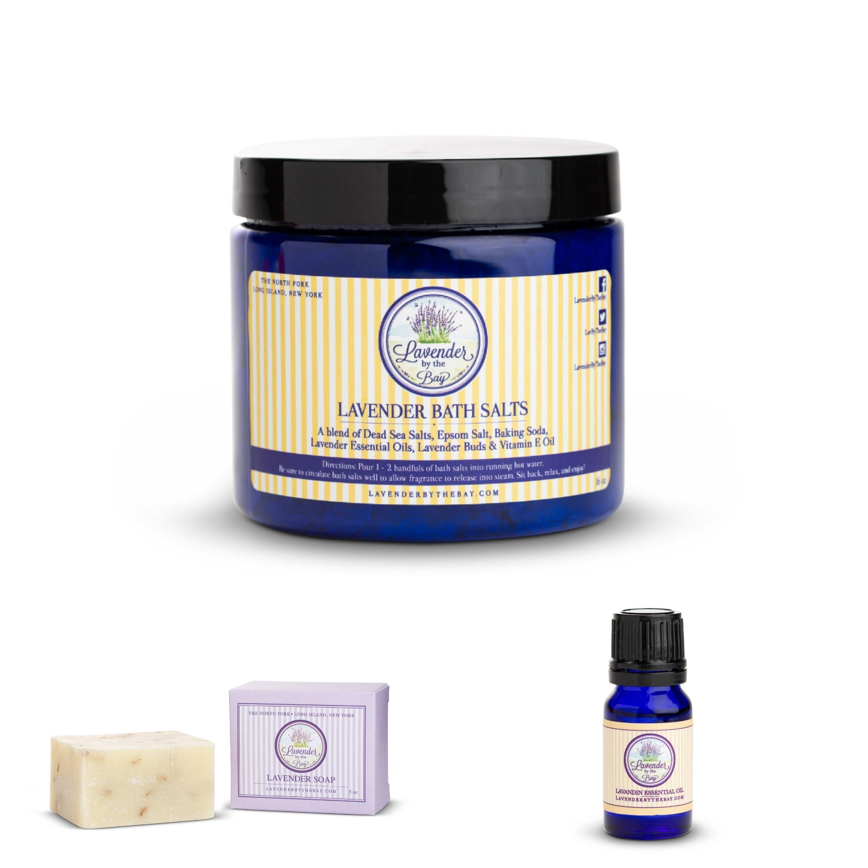 Image of the LBTB bath set featuring a plastic jar filled with lavender bath salts next to it lavender bar soap, and a small glass bottle filled with liquid with a label says Lavandin essential oil.