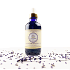 the Lavnder By The Bay Lavender Massage Oil blue bottle on white background with Lavenders flowers spread around the bottle