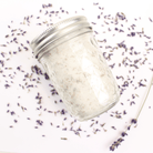 A glass jar filled with Lavender Sugar, surrounded by dried lavender flowers.