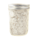 A clear glass jar with a silver lid, filled with white lavender sugar.