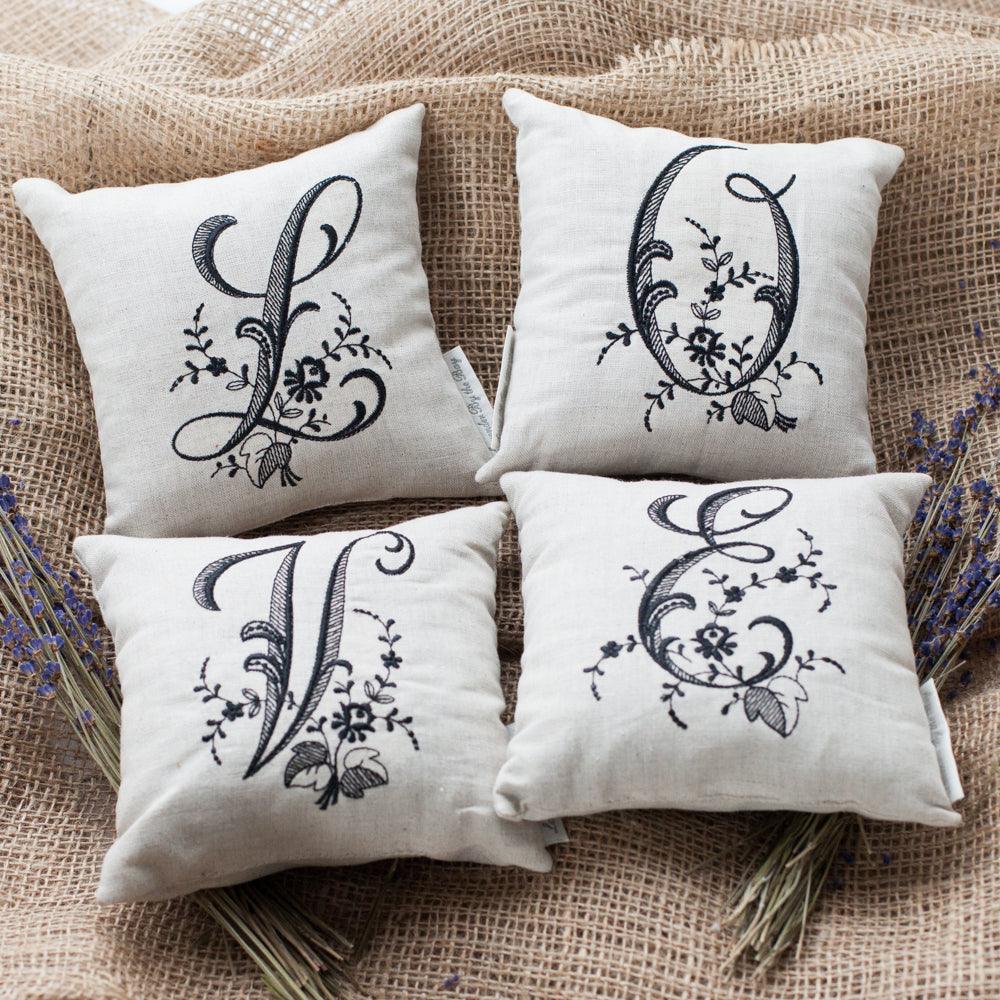 4 monogrammed pillows L Q V and E letters laying on burlap sack with 2 lavender bouquet from each side