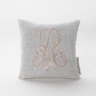 A luxurious monogram bed pillow. The pillow features a beautifully embroidered monogram of the letter "R," adorned with delicate floral patterns and swirling flourishes. The intricate stitching and elegant design make this pillow a timeless addition to any bedroom décor.