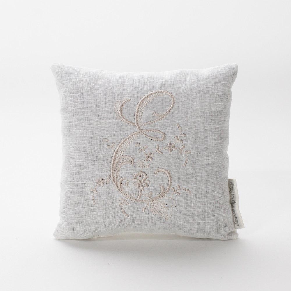A luxurious lavender pillow sachet. The sachet features a beautifully embroidered monogram pillow with the letter "E," adorned with delicate floral patterns and swirling flourishes. The intricate stitching and elegant design, combined with the calming scent of lavender, make this pillow sachet a perfect addition to any bedroom or closet.